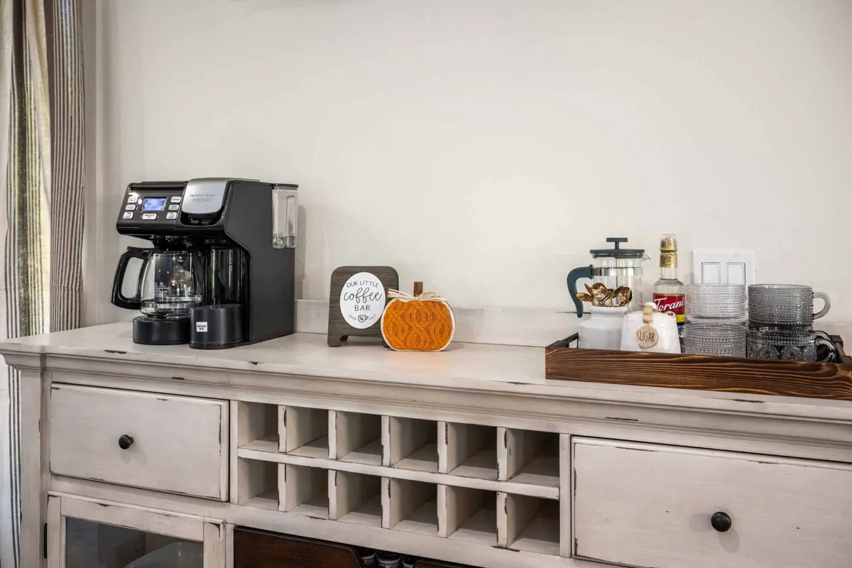 A welcoming coffee bar setup with a modern coffee maker, glassware, and a decorative sign, creating a cozy nook perfect for morning conversations or unwinding with a warm drink. Thoughtful details add seasonal charm and personality.