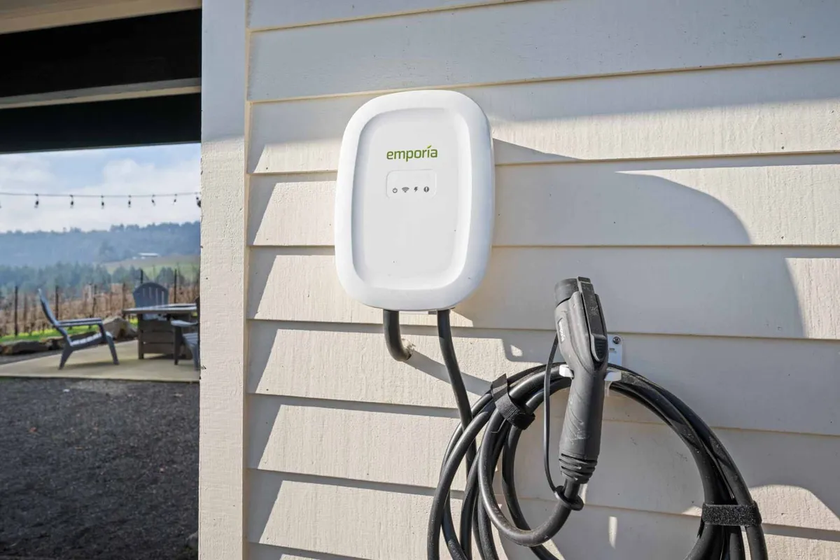 An exterior view centered on a modern EV charging station in front of the vineyard, with the charging cable visible and the lush grapevines stretching into the background. The scene is bright and open, blending eco-friendly amenities with scenic rural charm.