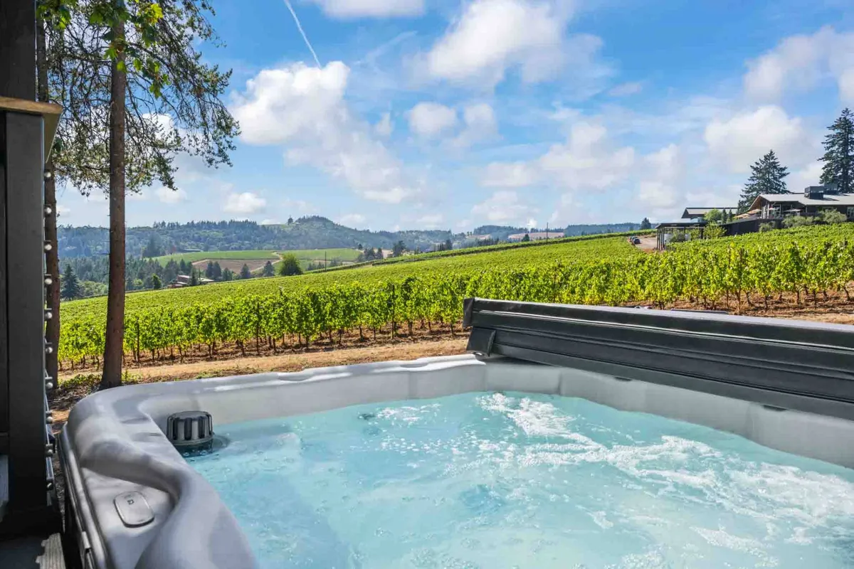 A serene outdoor scene featuring a recessed hot tub set into a wooden deck, overlooking a vineyard and distant rolling hills. Soft evening light and subtle landscaping add to the tranquil ambiance, emphasizing relaxation and scenic enjoyment.
