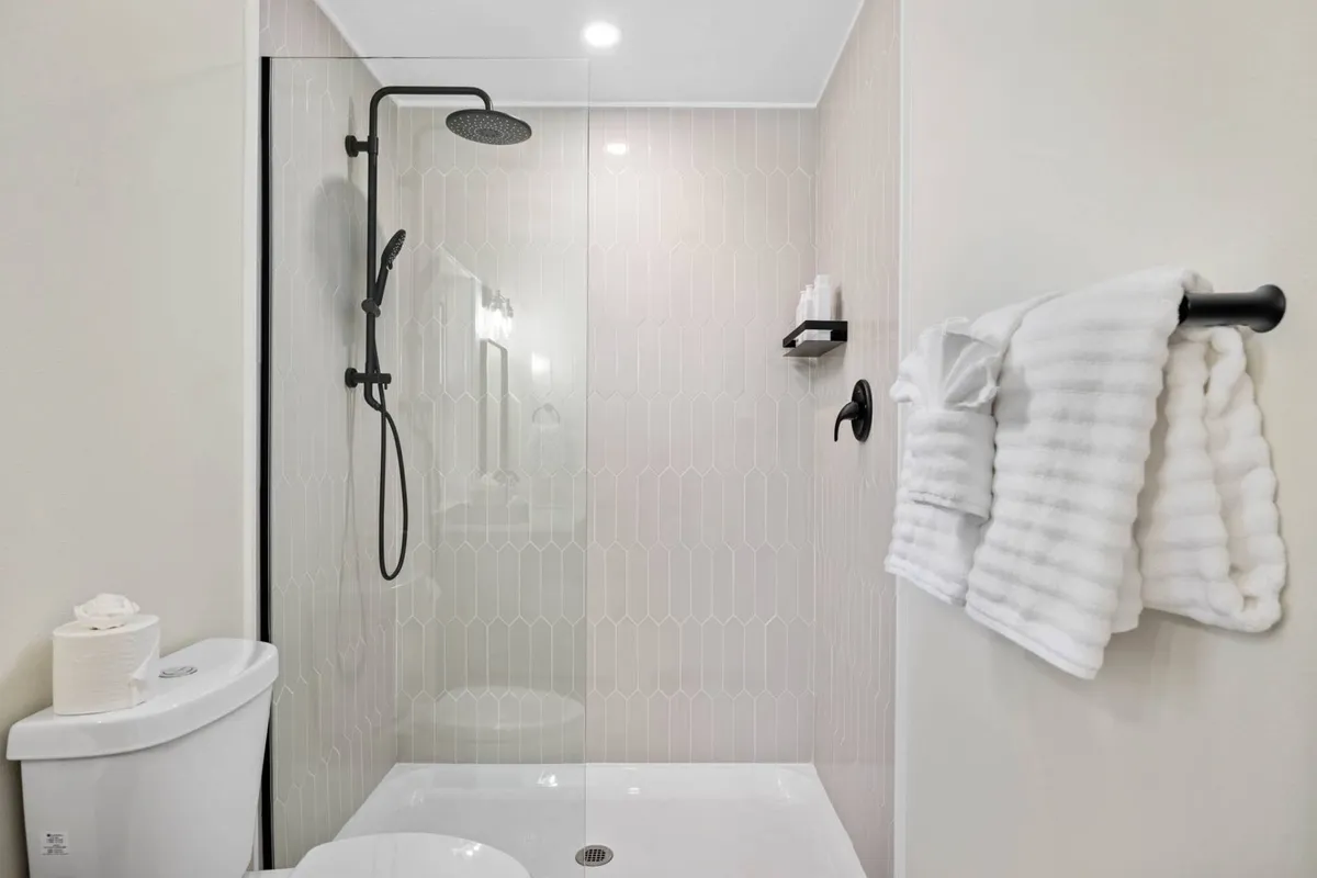 A serene and modern bathroom featuring a glass shower enclosure, textured wall tiles, and fluffy white towels. The space is designed for relaxation and self-care, with premium fixtures and a calming atmosphere.