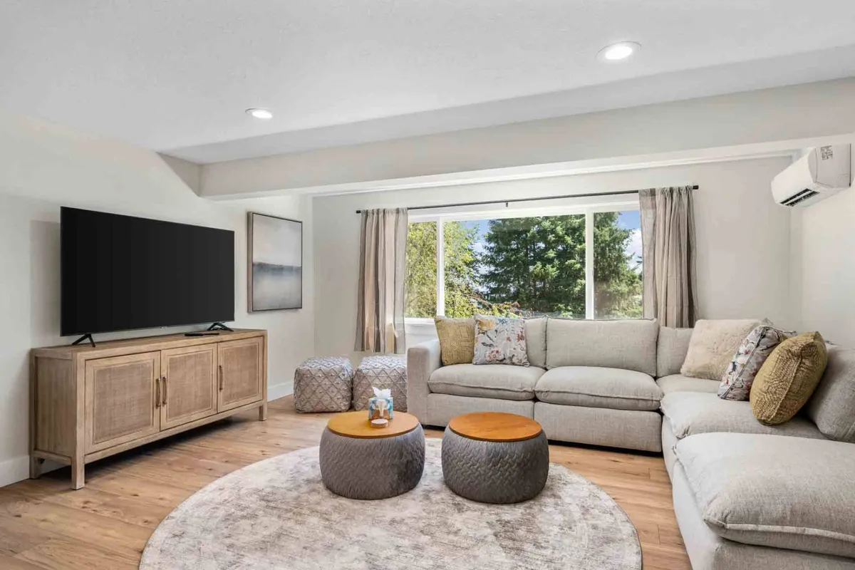 A spacious, comfortable entertainment lounge featuring a large sectional sofa, round coffee table, and a sleek TV unit with a flat screen. The room is filled with natural light from a generous window, creating an inviting space to relax, watch movies, or connect with friends and family.
