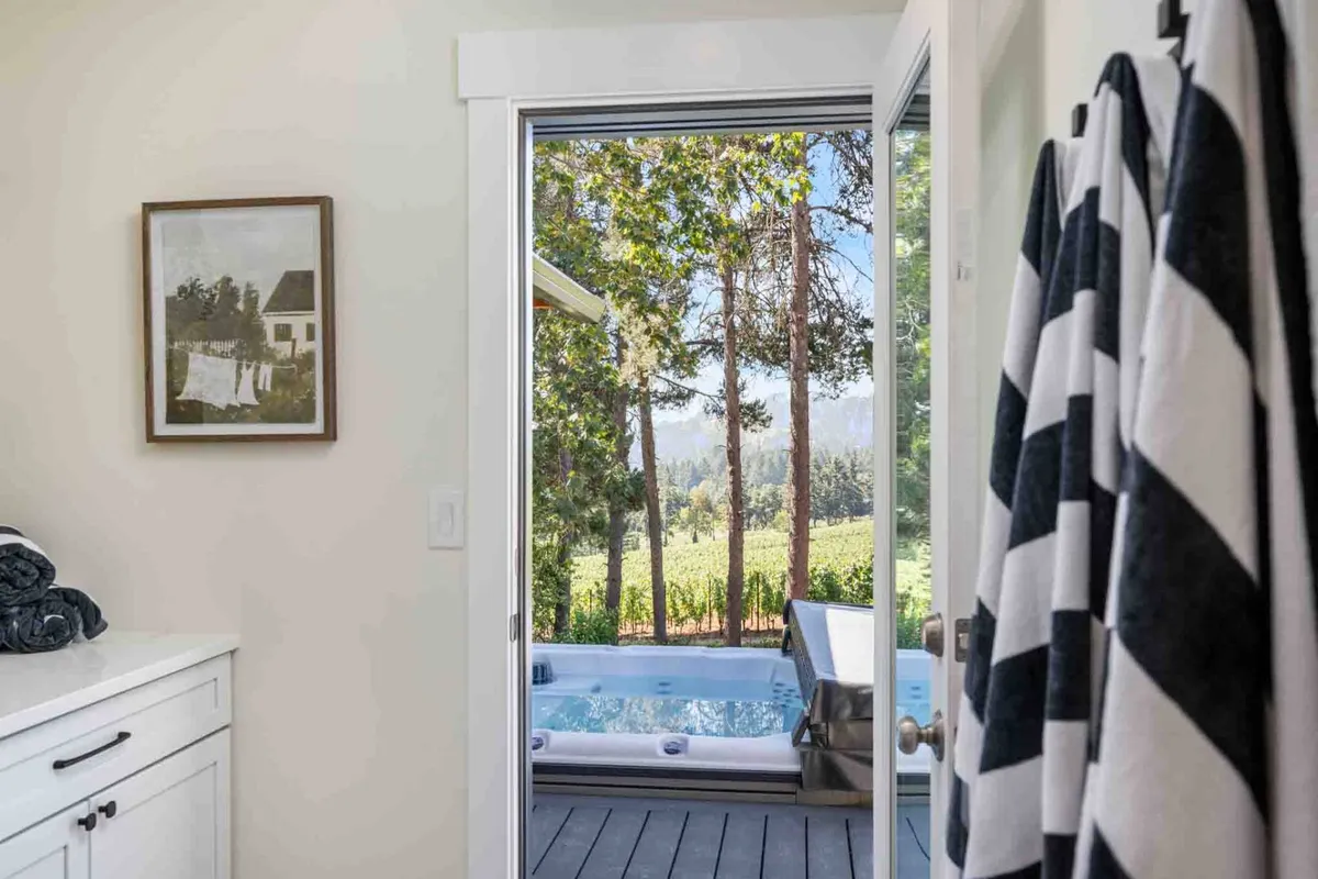 A serene interior perspective showing a jacuzzi placed by a window with sweeping vineyard views, complemented by local artwork. The setup offers a tranquil space for relaxation after exploring local wineries, with visual cues to both comfort and the surrounding landscape.