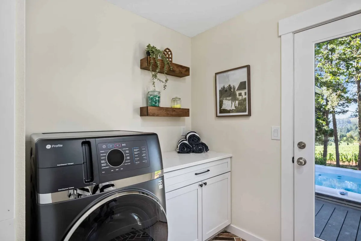 A tidy laundry and mudroom area with washer/dryer, shelves adorned with plants and decor, and a window providing a glimpse of the outdoors. The space feels functional and inviting, perfect for prepping for a day out or coming back from an excursion.
