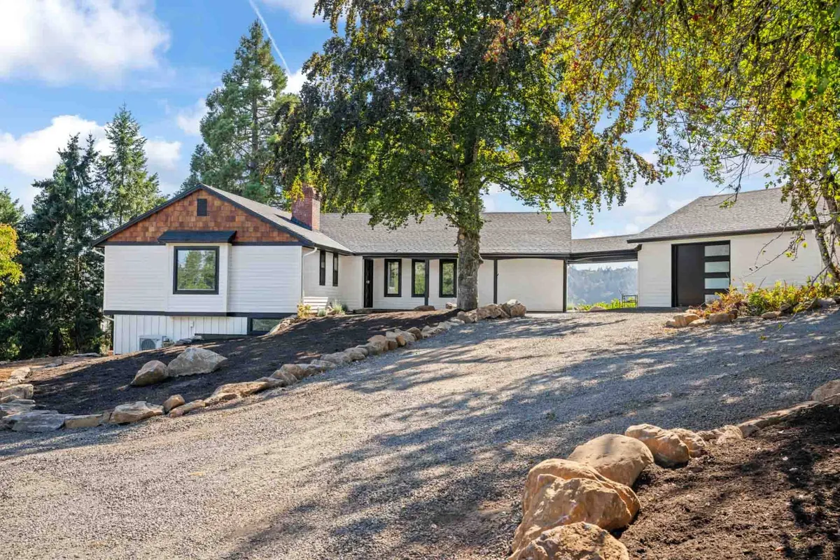 The image shows the exterior of Courtyard Cottage, surrounded by mature trees and beautifully landscaped grounds. The spacious driveway leads up to the home, and the setting sun bathes the scene in a warm, inviting glow, suggesting a tranquil yet lively place for arrivals and outdoor fun.